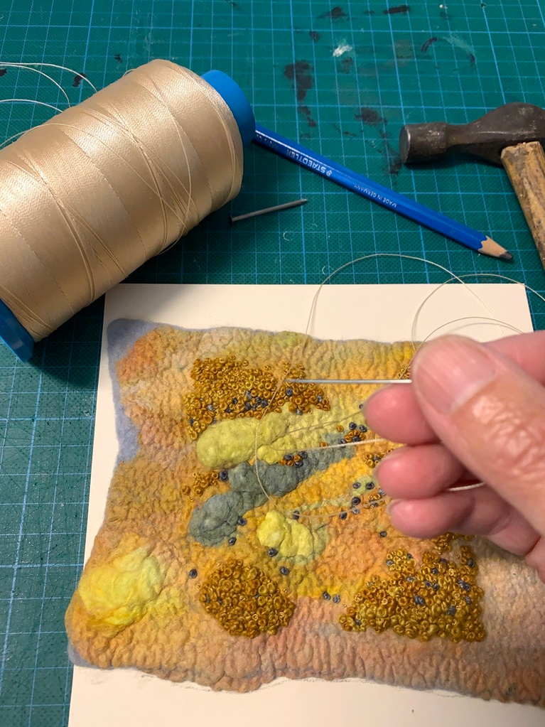 Thread a needle with upholstery thread and string the felt artwork onto conservation board 