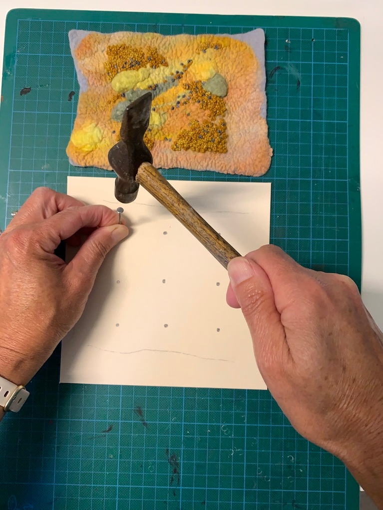 Lynn Comley felt artist hammers holes into a card to string the work onto