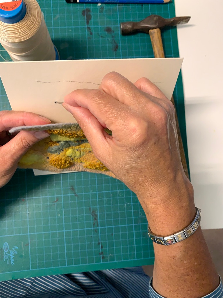 Thread the needle through the backing mount board and secure the wet felted artwork