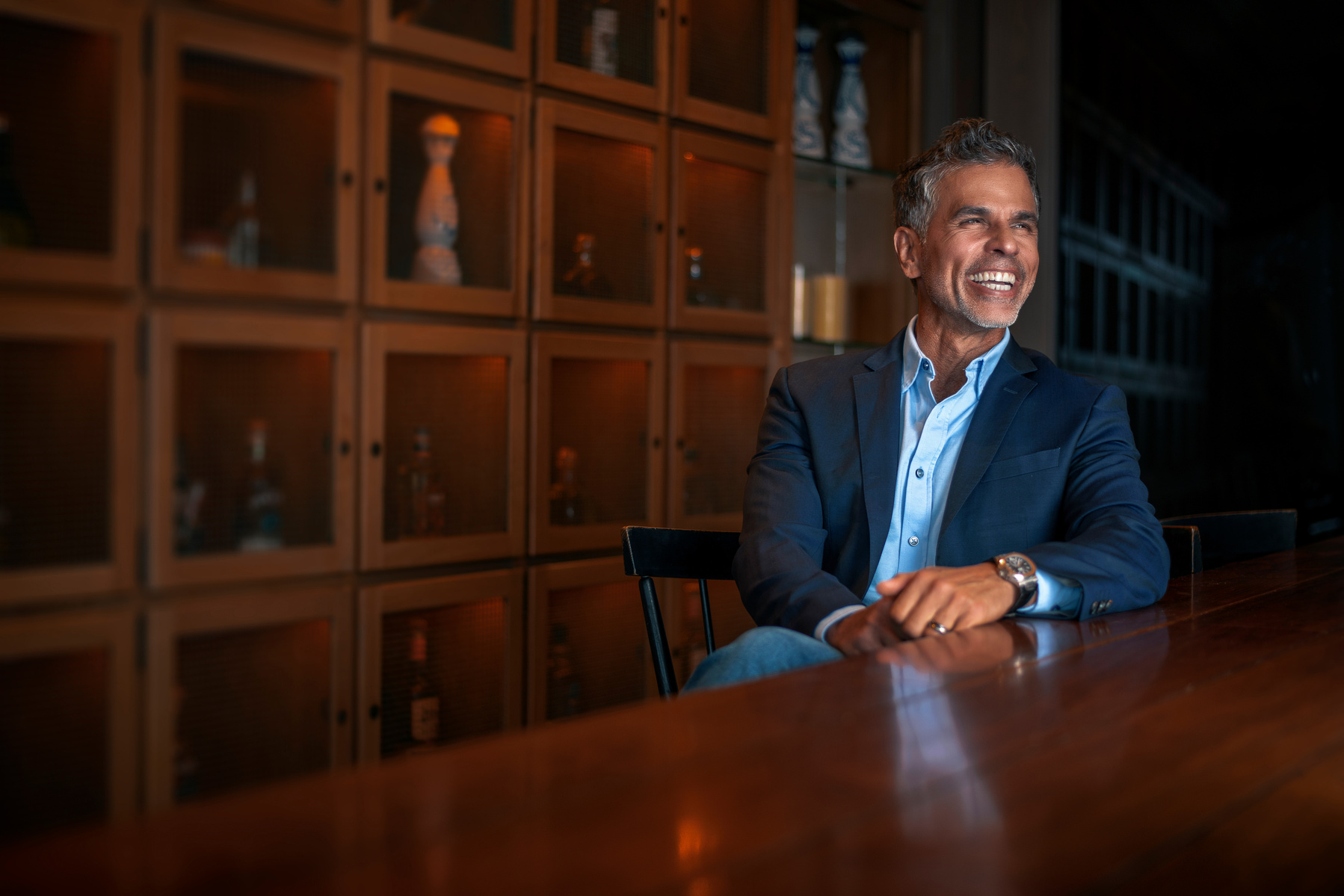Man in a suit laughing at a wooden table and masculine furnishings 