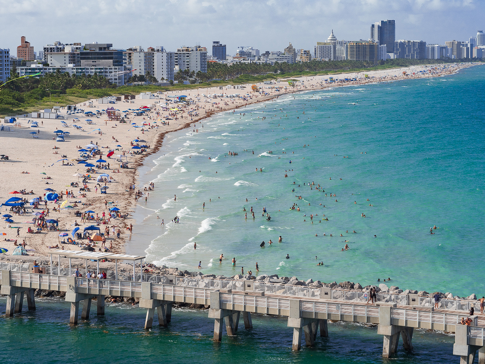 Bustling Miami beach and pier, with vibrant umbrellas, azure waters, and cityscape.