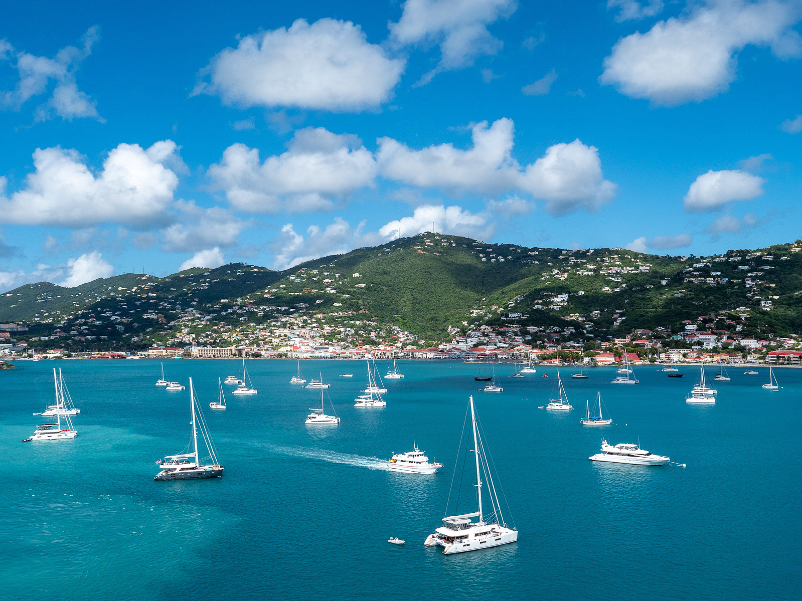 Yachts dot the serene blue waters of St. Thomas with lush hills under a sky streaked with clouds.