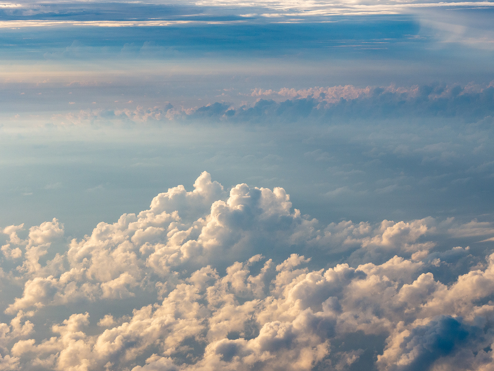 Fluffy cumulus clouds bask in the golden light of the setting sun, seen from an aerial perspective.