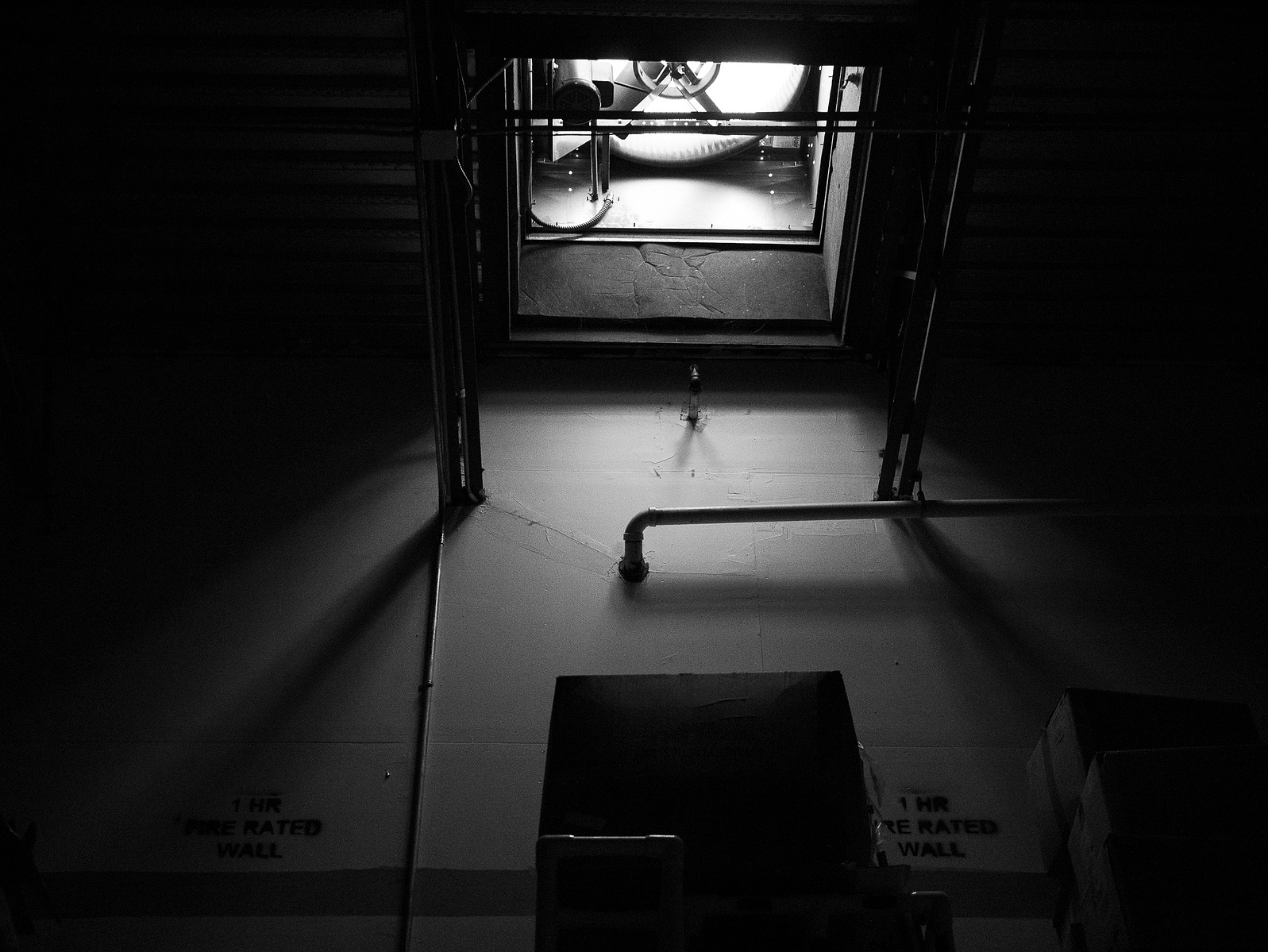 A black and white image capturing stark contrasts where a single light source casts intriguing shadows in an industrial setting.