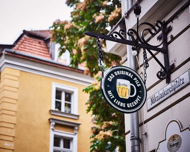 A round sign advertising beer handing outside a pub in Berlin. A yellow building can be seen inthe background, echoing the yellow in the drawing of the beer