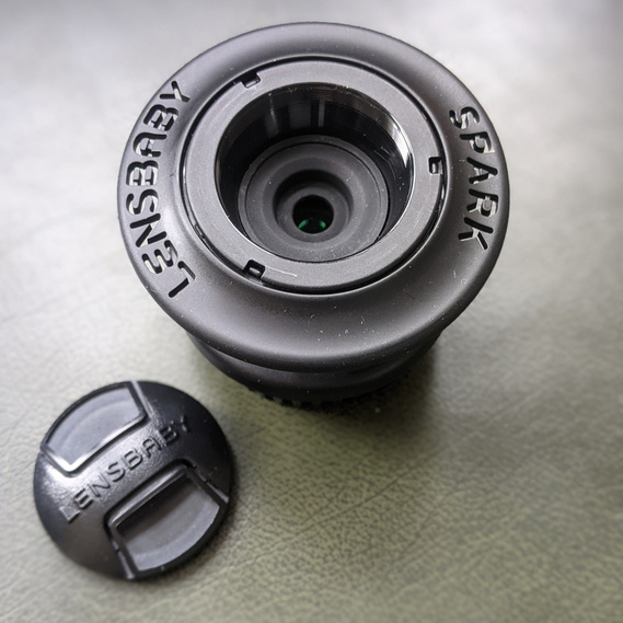 Overhead shot of the Lensbaby Spark without the lens cap. The cap sits next to it. 'Lensbaby Spark' is written on the ring of the lens