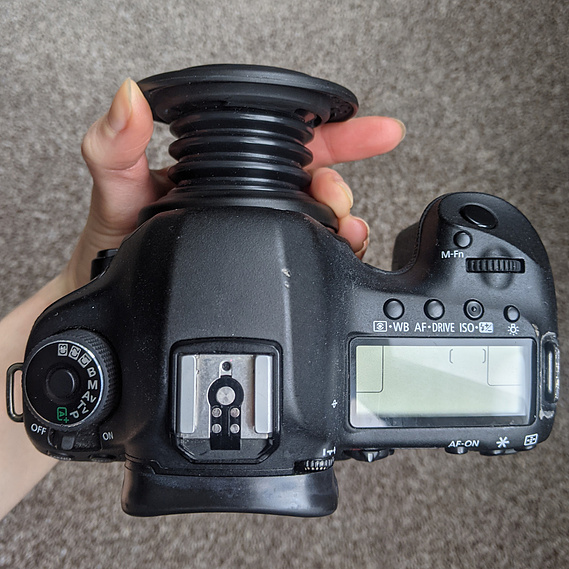 Lensbaby Spark mounted onto the camera. A hand supports the camera and pulls outer rim of the lens so you can see how it pulls away from the camera to choose focus points