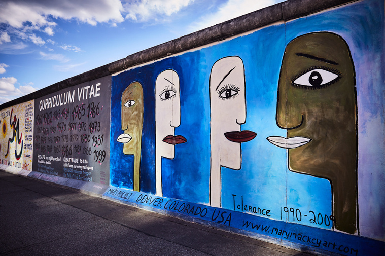 Artwork at the East Side Gallery by artists (L-R) Jolly Kunjappu, Susanne Kunjappu-Jellinek, Mary Mackey. The main image shows 4 peoples faces who each have different skin colours. 