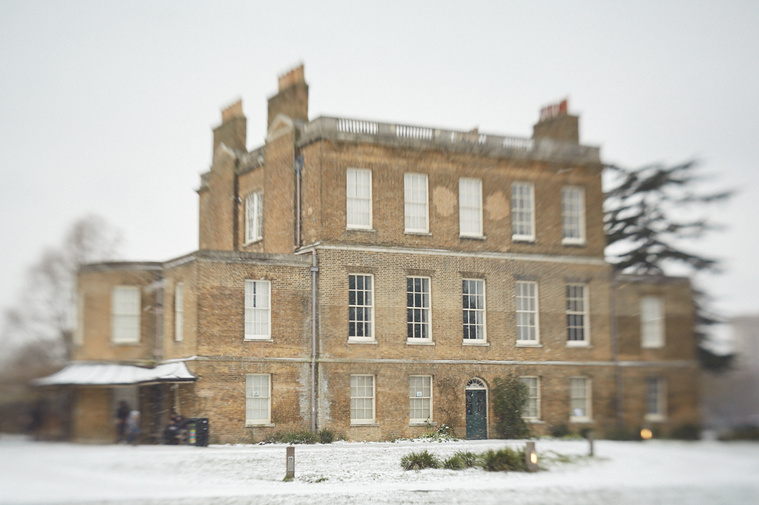 A grand house with many windows and chimneys. There is snow on the ground and the edges of the frame are soft - a creative effect of the Lensbaby Spark
