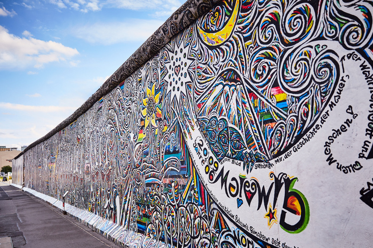 Multicolour mural at the East Side Gallery by artist Schamil Gimajew titled Worlds People. Within the mural are stars, faces and flowers outlined in black