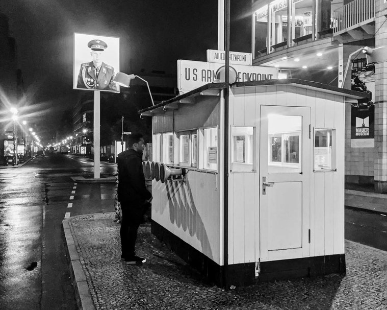 Check-point Charlie in Berlin, a famous landmark within the city which was an old border crossing separating East and West Berlin. A large photograph of a solider is visible behind a white hut, upon the hut a sign reads 'US army checkpoint'