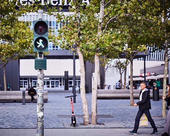 Ampelmann, Germanys unique road crossing icon in green can be seen on a traffic light across the road. A main walking past has been captured in the same position, with his legs striding and his arm in front