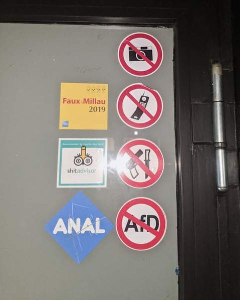 Signs on a non-descript door that symbolise 'no photos, no phones, no knives or guns and no AfD'. AfD is a german right-wing political party. Other stickers read 'Anal' and another reads 'ShitAdvisor', with a penis on the head of the Trip Advior Owl logo.