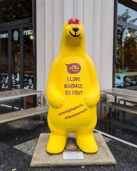 A large yellow bear with a red crown invites you into The Big Dog hotdog restaurant, on his chest, it says 