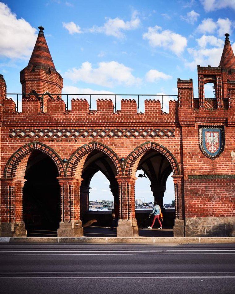 A person in red trousers walks through the Oberbaum Bridge, their trousers echoing the colour of the brickwork