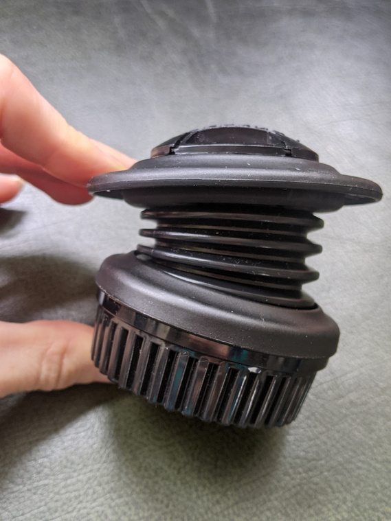Lensbaby Spark shown unmounted to a camera. A visual demonstration of an index finger pressing down on the top rim, towards the camera mount, showing how flexible the  lens is and its ability to push towards the camera (if it was mounted)