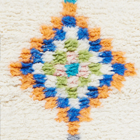 Close-up shot of a Moroccan Berber rug showing the piling and texture. The pattern is orange, blue and green squares