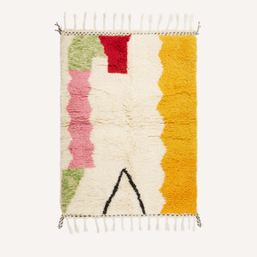 A handmade Moroccan Berber rug with tassels at the top and bottom, a block of orange to the left of the rug, cream in the centre and red, pink and green to the right