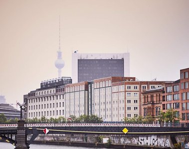 Marschall Bridge runs horizontally across the frame with a view of the Berlin TV Tower. It's rainy and hazy in the distance, with the TV Tower appearing washed out by the haze.  A cold looking River Spree can be seen in the foreground