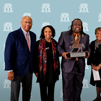 Brenda and Larry Thompson Award - Georgia Museum of Art- Five People in Professional Wear Posing for a Picture With a Man in the Middle with an Award in His Hand. The Background of The Picture is Pale Blue with a White Logo.