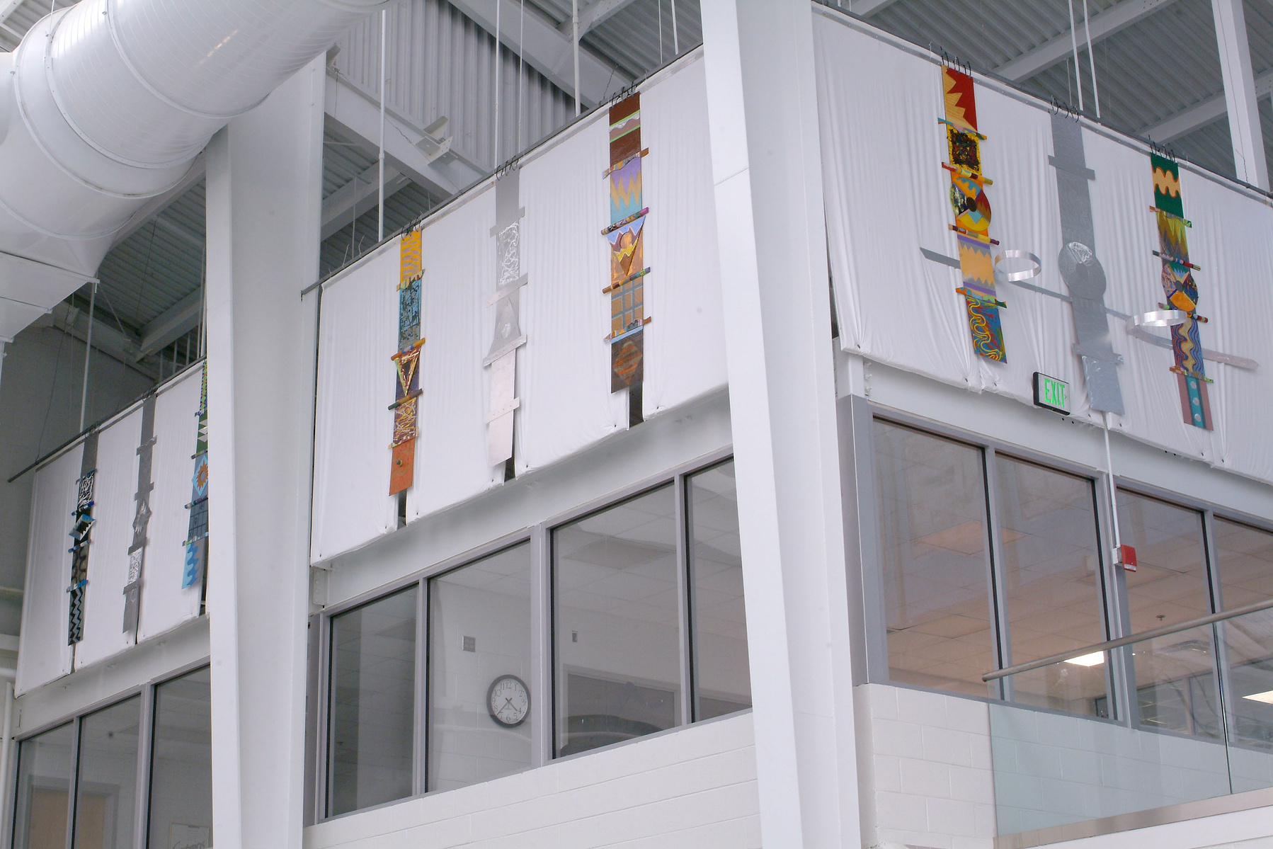 Totems For Maynard Washington Park Natatorium, Installation Atlanta, GA-Multiple totems that are multi-colored hanging on a wall close the ceiling in a Natatorium.