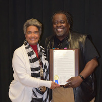 Proclamation from The City Of Atlanta- A Man and A Woman Posing for a Photo in Causal Wear. The Man on the Right is Holding a Sheet of Paper.