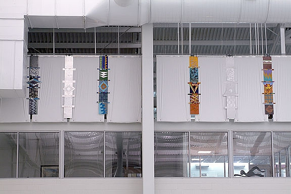 Totems For Maynard Washington Park Natatorium, Installation Atlanta, GA-Multiple totems that are multi-colored hanging on a wall close the ceiling in a Natatorium.