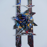 Midnite Prayers-Abstract cutout art piece on paper that resembles ladder  which has a circle in the middle. The colors of the piece are mostly black with multicolor splatters.