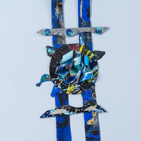 Silent Moment-Abstract cutout art piece on paper that resembles ladder  which has a circle in the middle. The colors of the piece are mostly blue with gray and hints of green.
