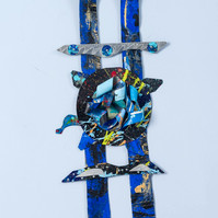 Silent Moment-Abstract cutout art piece on paper that resembles ladder  which has a circle in the middle. The colors of the piece are mostly blue with gray and hints of green.