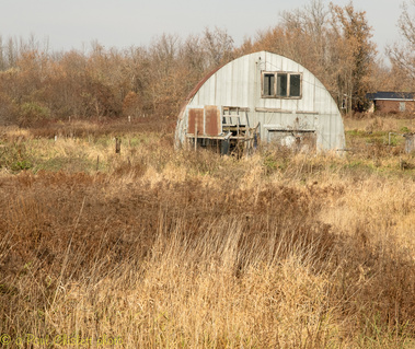 A slightly run down Quonset hut sits amid a field of brown and yellow grass.