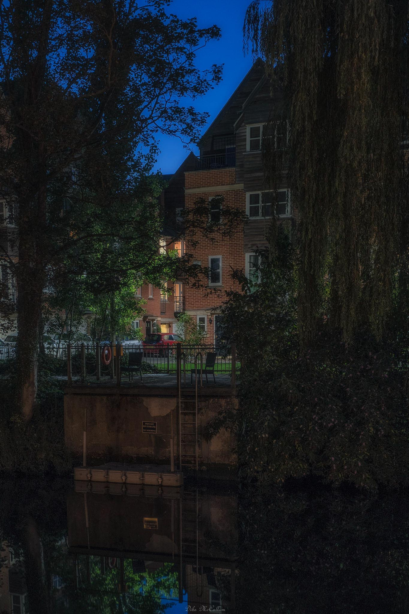 Looking over the river Wensum at blue hour from quayside to fishergate apartments in Norwich Norfolk as a little bit of light illuminates a house through the trees