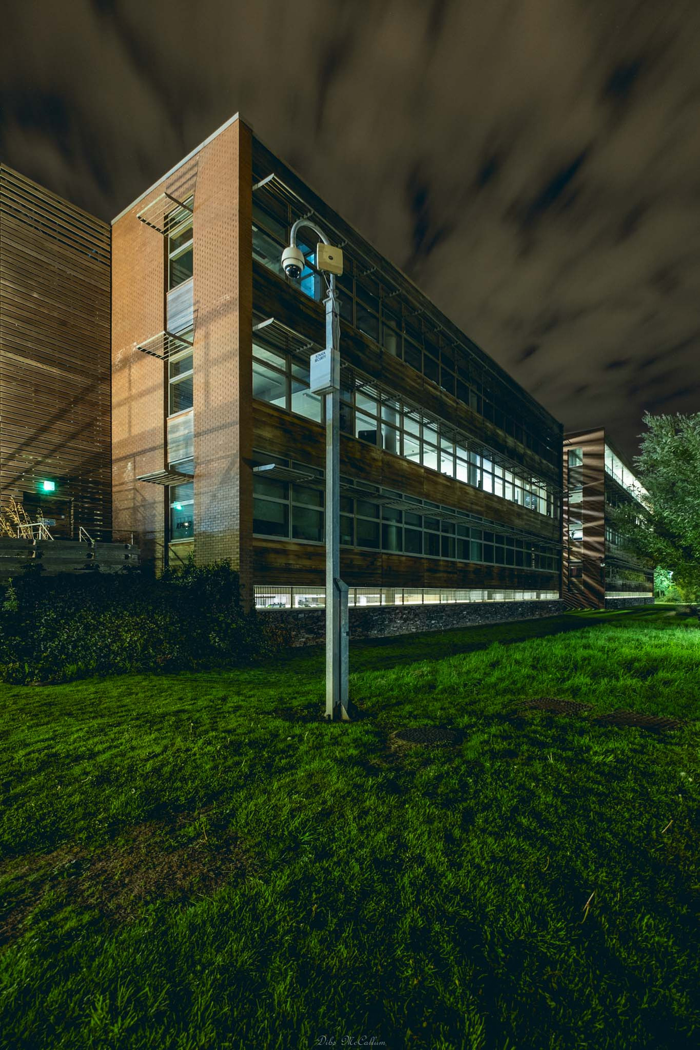 Night time photo of Dragonfly House in Norwich Norfolk with the green grass in front of it and the sky orange colour and the building illuminated by the nearby lighting