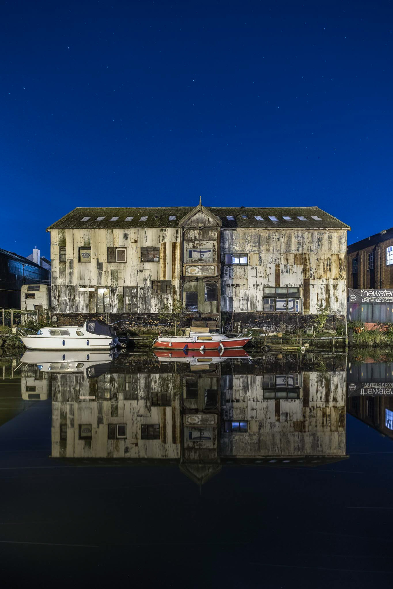The A.B.C wharf on Norwich Riverside at night, with a decaying boat and its reflection in the water