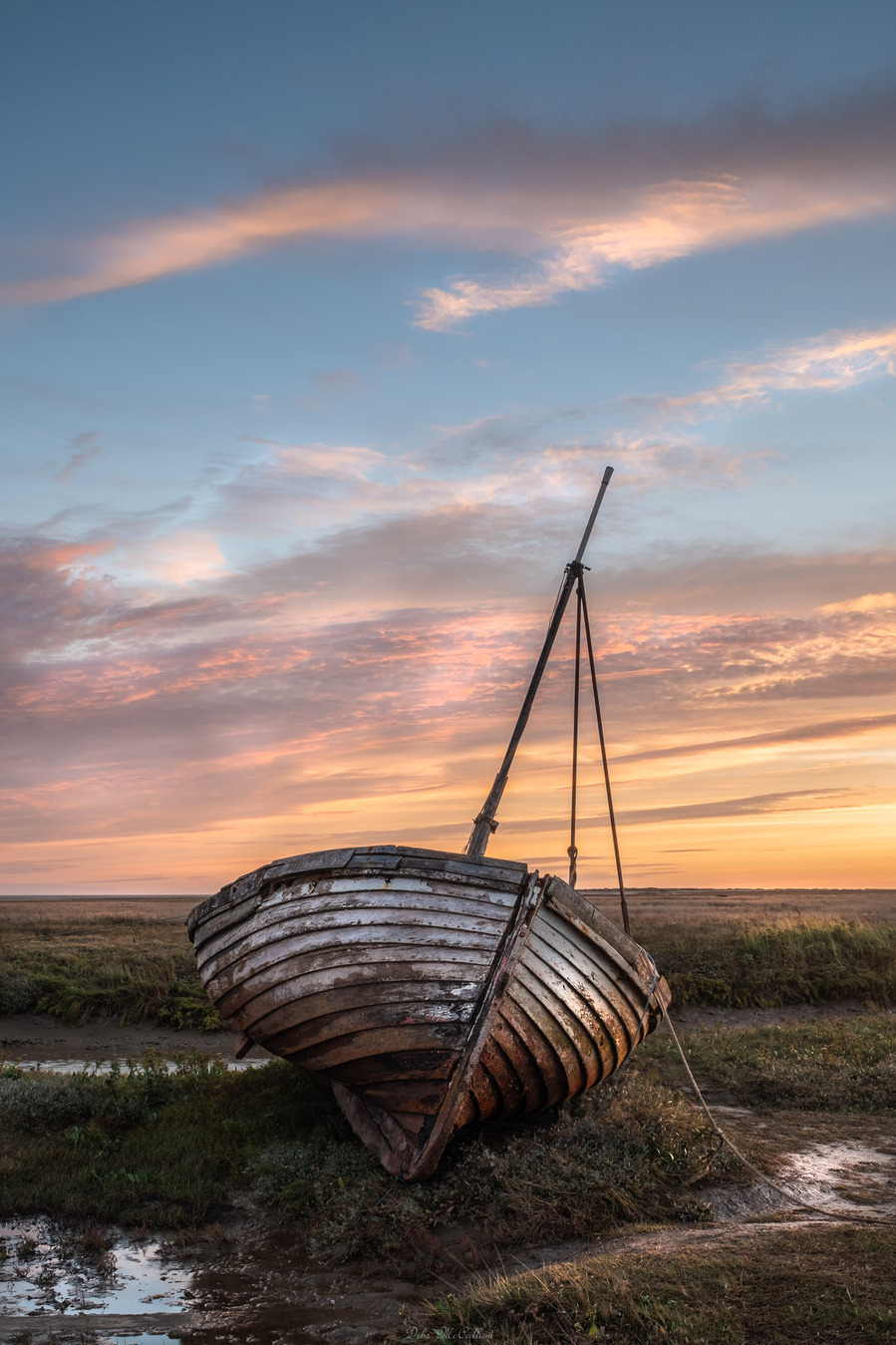 decaying white sailboat with peeling paint with a red sky and clouds at sunset on the Norfolk coast