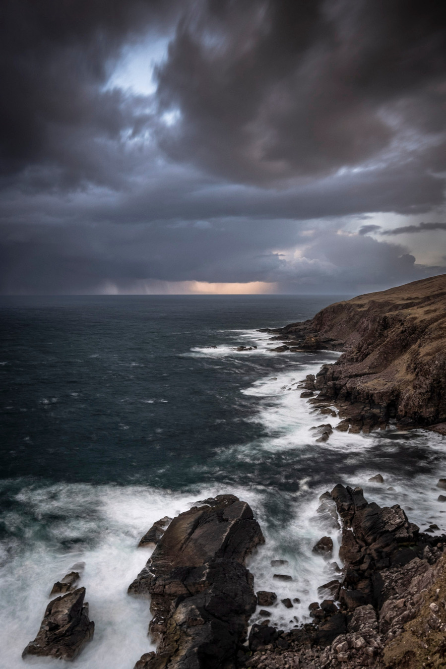 Scenic view of rugged rocks with crashing waves and a moody sky in North Scotland.