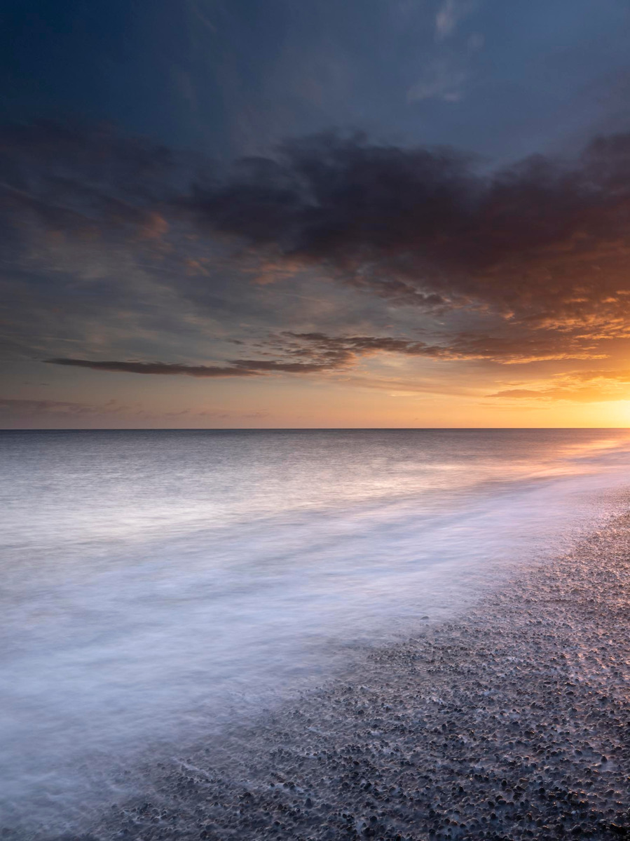 Golden sunrise on the beach at Weybourne in North Norfolk with clouds illuminated by the sun and it reflects onto the water and the white waves