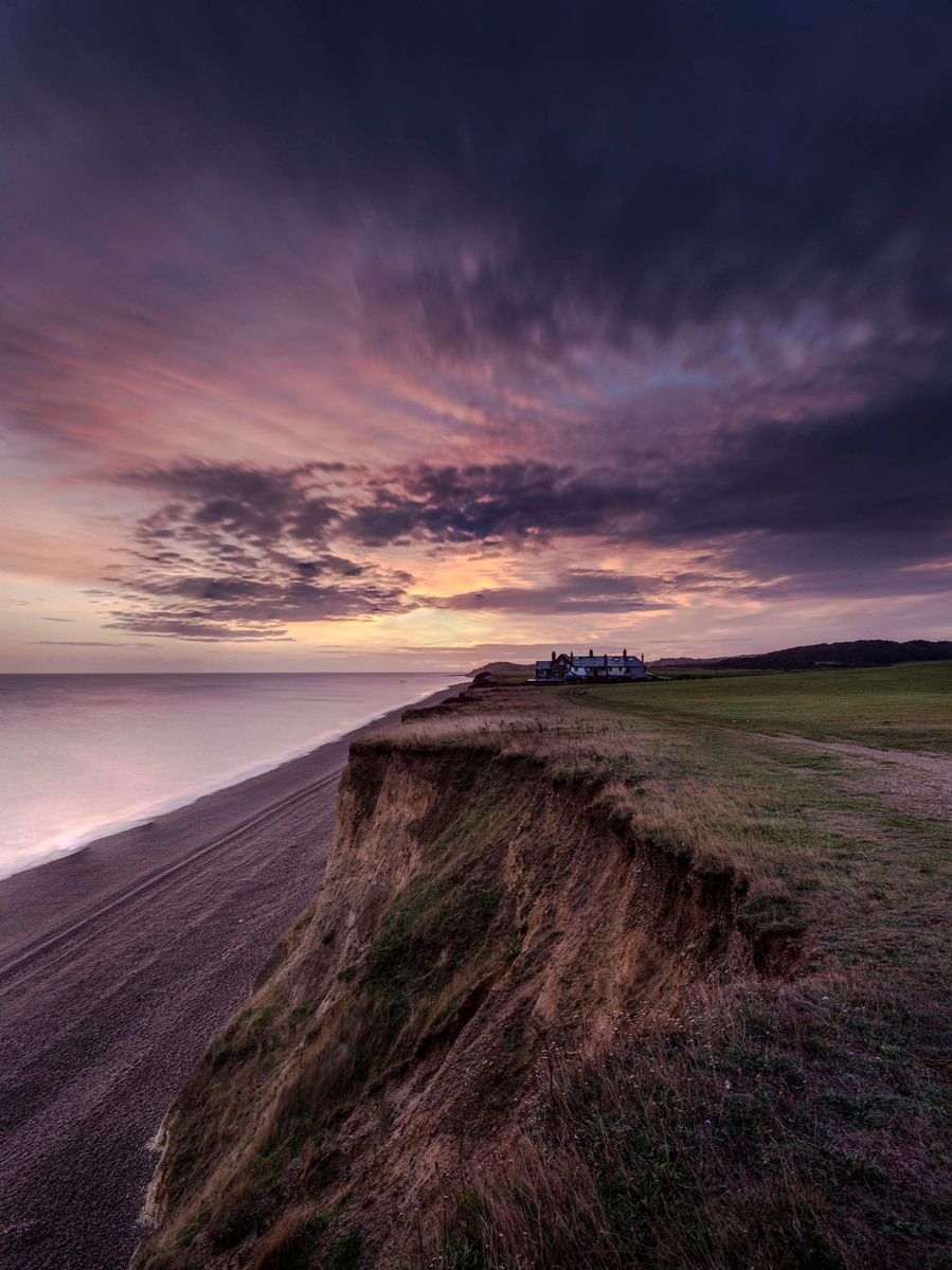 A lone house close to and on top of the eroding cliffs of Weybourne in Norfolk with a fantastic sunrise making the sky and water turn a red and purple colour
