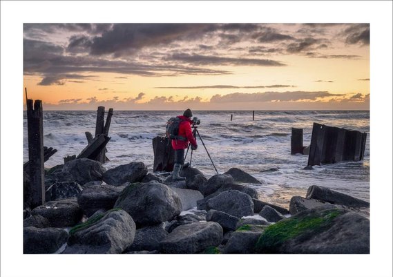 Landscape Photographer stood on rocks at sunrise in red jacket with wellies