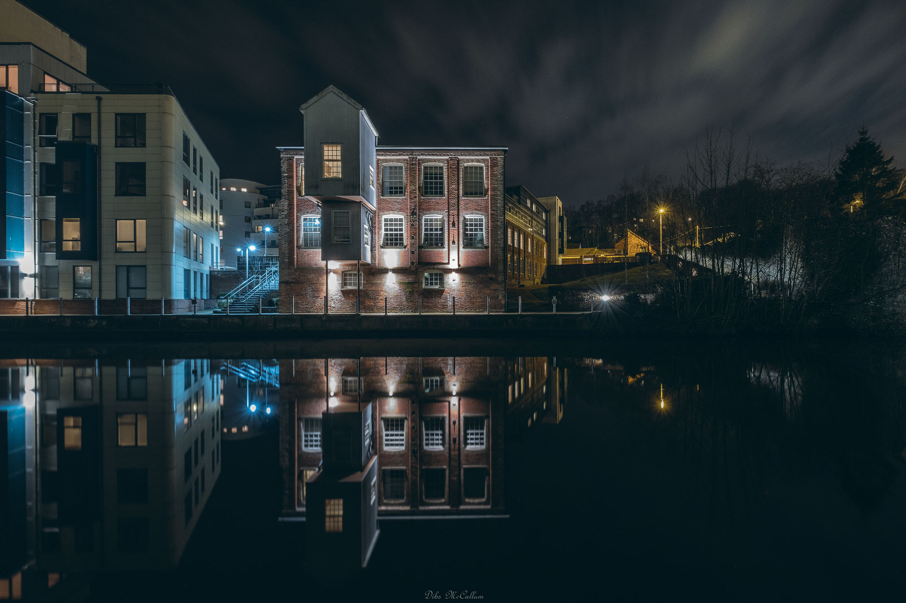 Old mill on the river Wensum in Norwich Norfolk at night with a clear reflection on the calm water and clouds in the sky