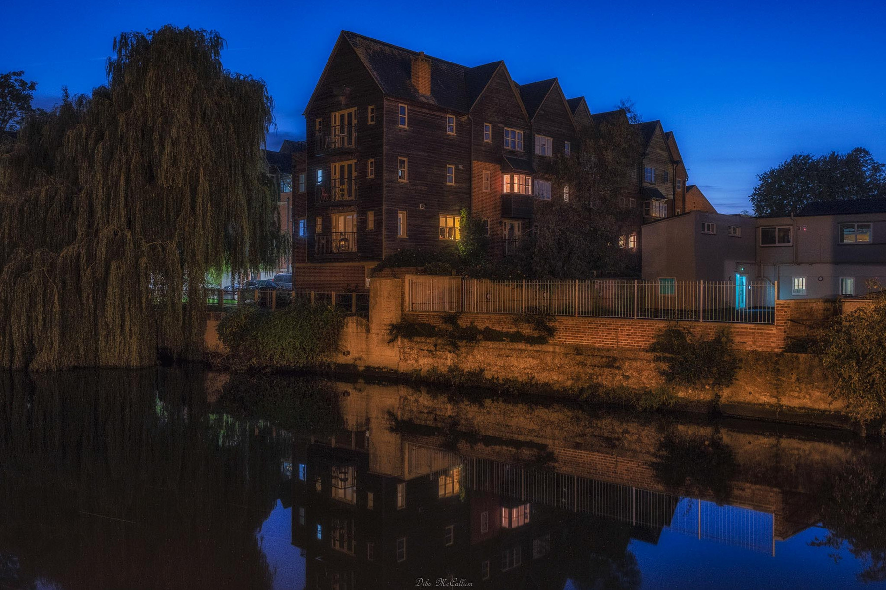 Looking over the river Wensum at blue hour from quayside to fishergate apartments in Norwich Norfolk as a little bit of light illuminates a house through the trees