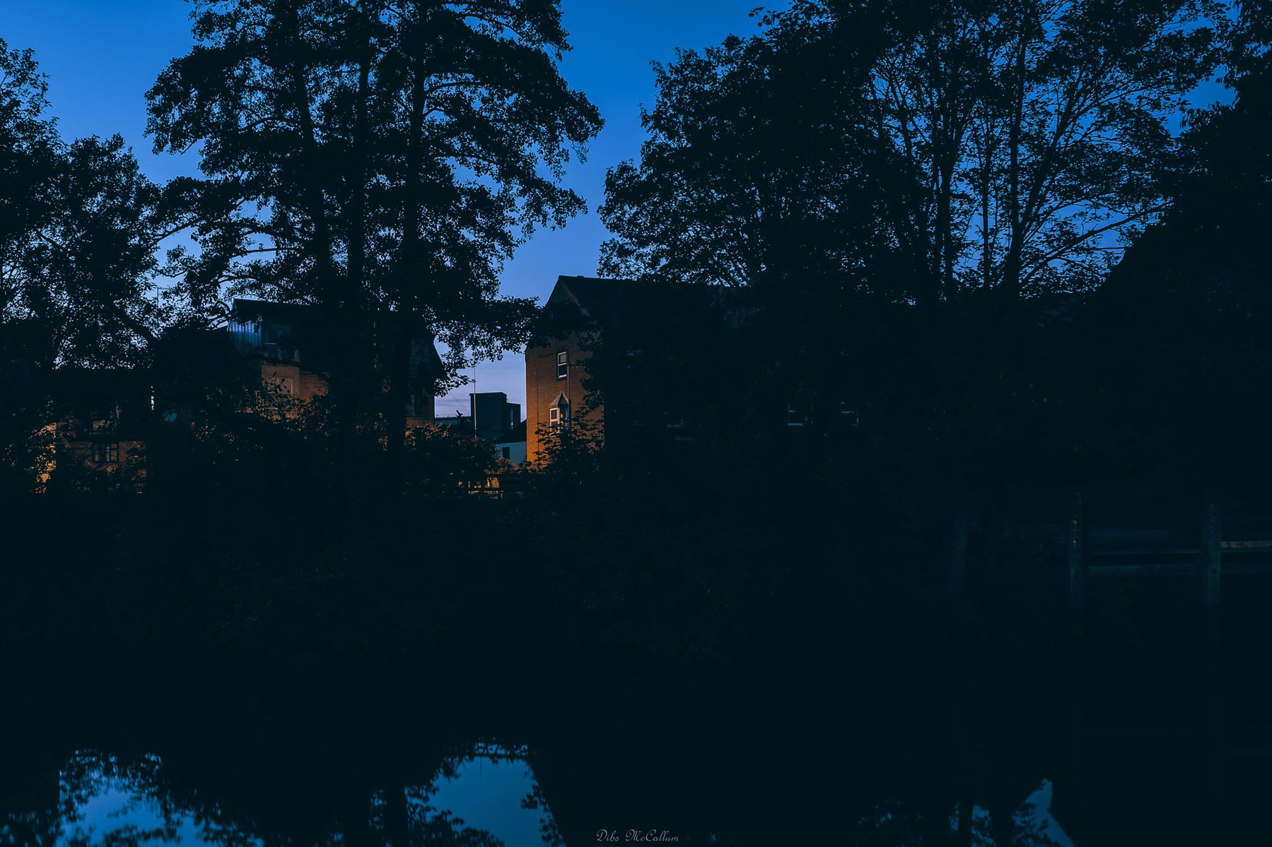 Looking over the river Wensum at blue hour from quayside to fishergate apartments in Norwich Norfolk as a little bit of light illuminates a house through the trees