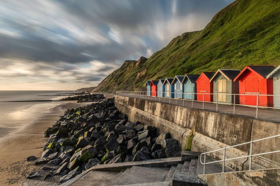 Multi-coloured beach on the sea front at Sheringham in Norfolk with amazing clouds and a blue sky with rocks on the beach on a sunny day