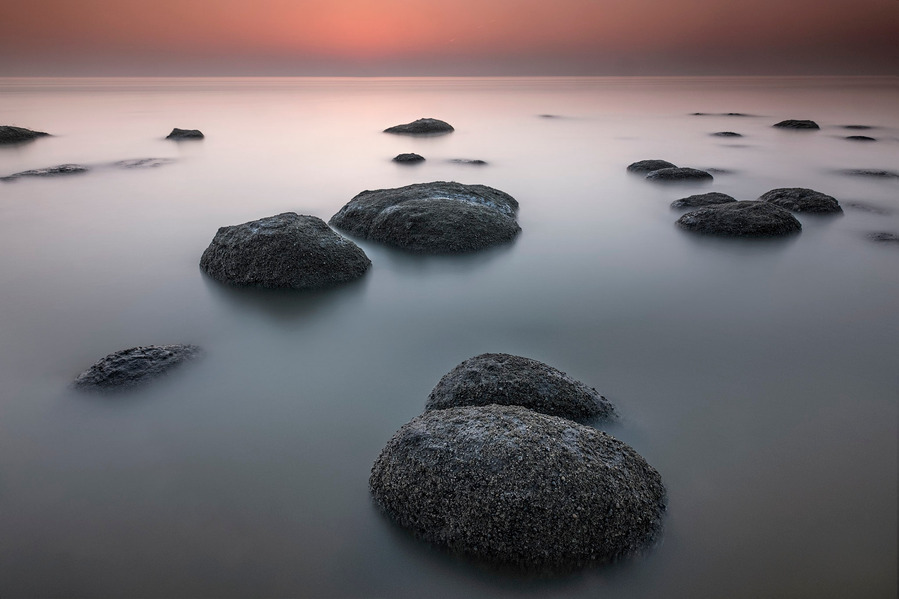 The rocks of Hunstanton in Norfolk at sunrise are half submerged by the sea just after high tide as the sunset glows red and reflects onto the smooth water created by a long exposure