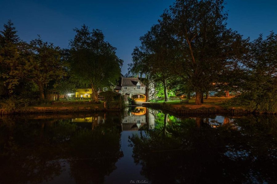 The iconic Pulls ferry illuminated at night that is part of Norwich cathedral on the river Wensum in Norfolk that is part of the Norfolk broads national park.
