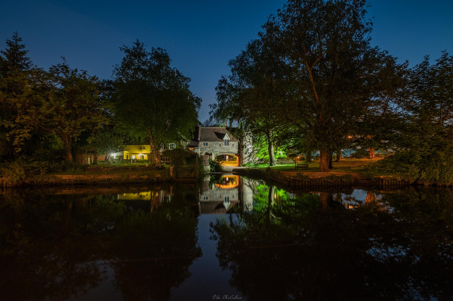 The iconic Pulls ferry illuminated at night that is part of Norwich cathedral on the river Wensum in Norfolk that is part of the Norfolk broads national park.

