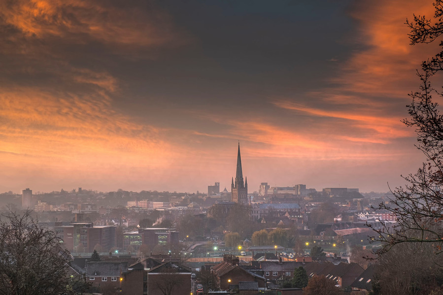 Cityview of Norwich city with the cathedral with a red sky and white clouds at sunrise on a cold morning