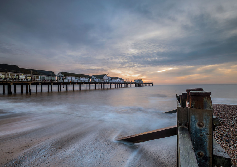 Southwold pier in Suffolk at sunrise with a  golden light in the sky photographed from one of the adjacent sea defences with it also in the frame as the sea moves along the beach creating whites on the sand
