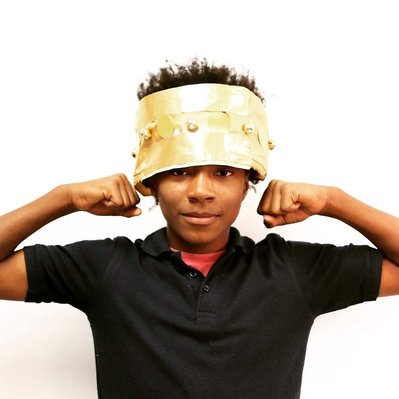 a Black boy wears a gold crown and shows his muscles to look strong
