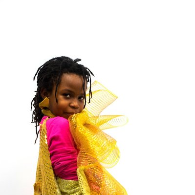 a Black girl wears a gold cape and hold gold fabric